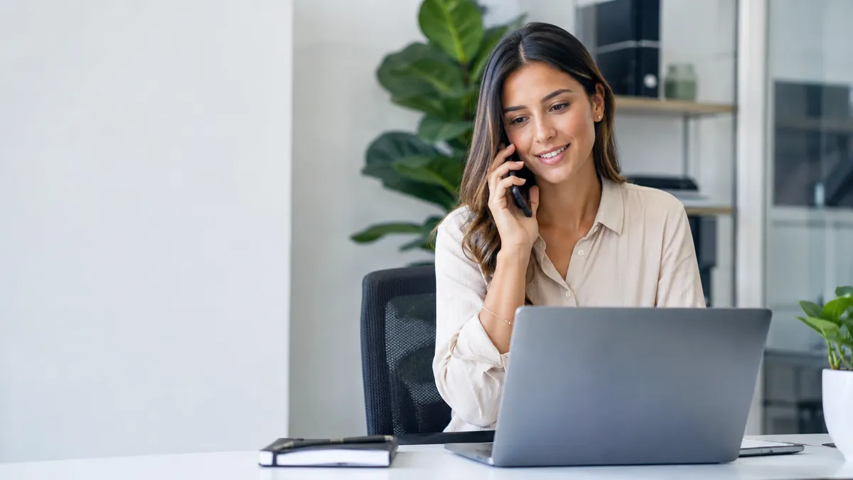 Asesora gestionando una conversacion con cliente desde telefono y laptop